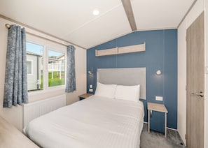 A bedroom with a bed, a window with curtains, a bedside table, and a nightstand.
