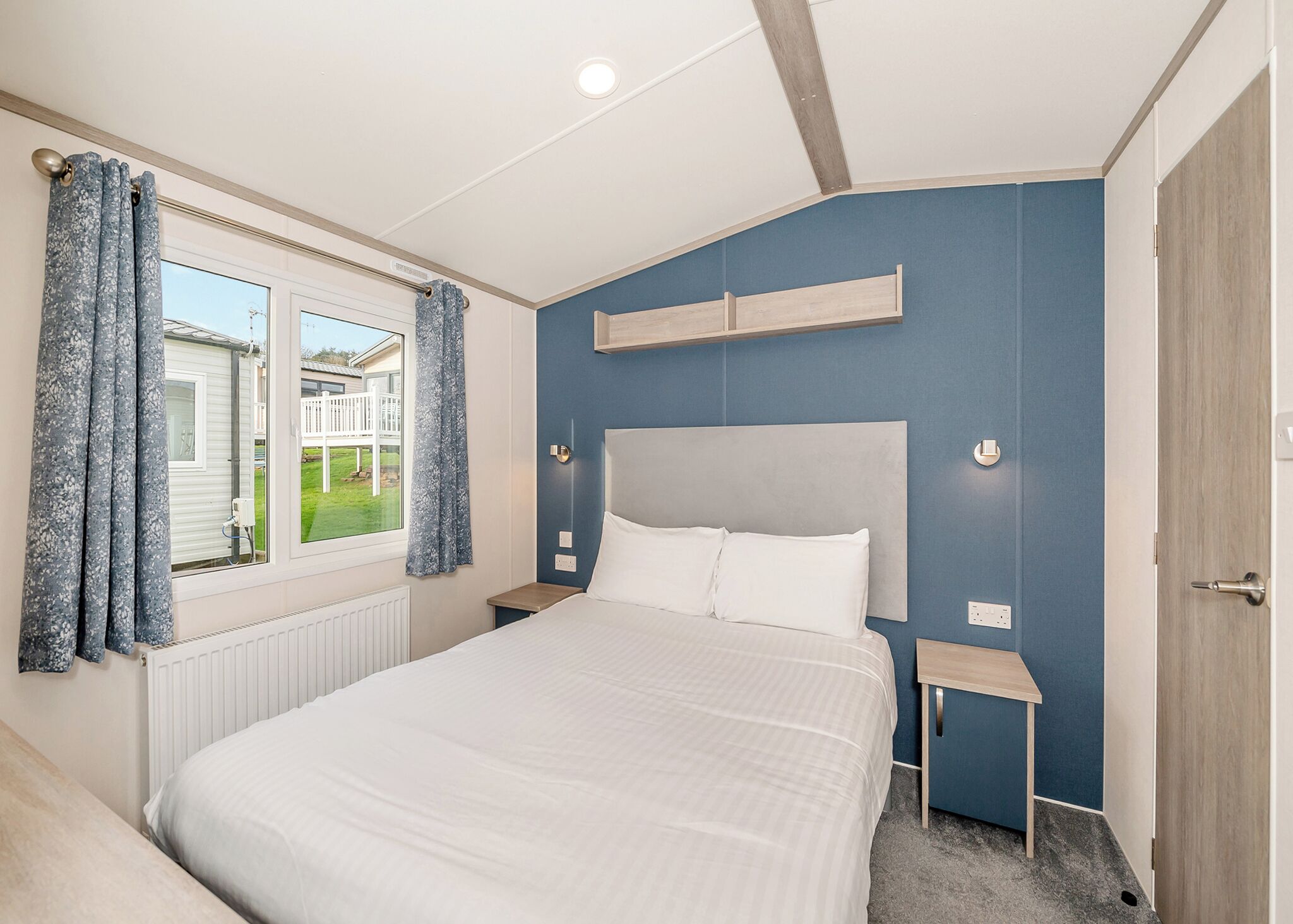 Um quarto com uma cama, janela com cortinas, mesa de cabeceira e criado-mudo.