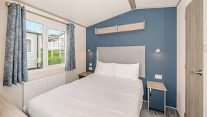A bedroom with a bed, a window with curtains, a bedside table, and a nightstand.