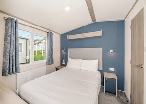 Une chambre à coucher avec un lit, une fenêtre avec des rideaux, une table de chevet et une commode.