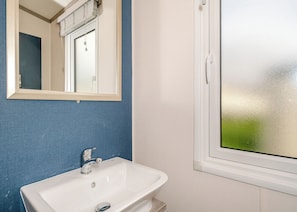 Une salle de bain avec un lavabo blanc, un miroir et une fenêtre.