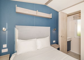 Un dormitorio con una cama, una mesita de noche, un estante en la pared, una puerta y una ventana.