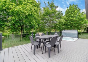 A deck with a table and chairs, a hot tub, and a view of trees.