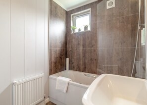A bathroom with a bathtub, a shower, a window with plants, and a radiator.