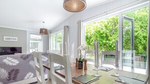 Ein modernes Zimmer mit Esstisch für zwei Personen, einem Fernseher und großen Fenstern mit Blick auf Grünflächen.