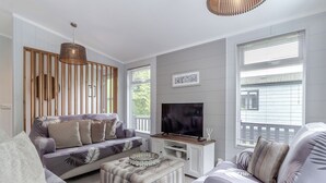 Ein modernes Wohnzimmer mit einer Couch, Hocker, Fernseher und großen Fenstern.