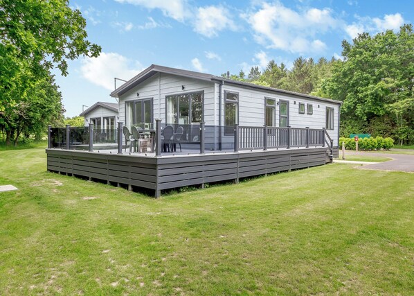 A modern mobile home with a deck, large windows, and a grassy yard.