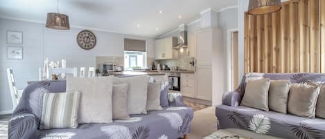 A modern living room with a sofa set, a dining area, and a kitchen.