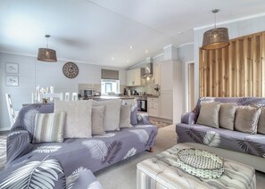 A modern living room with a sofa set, a dining area, and a kitchen.