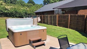A hot tub in a backyard with a wooden deck, a wooden fence, and a grassy lawn. - Lodge with fantastic contemporary styling. (Llanddewi, Nr. Llandrindod Wells)