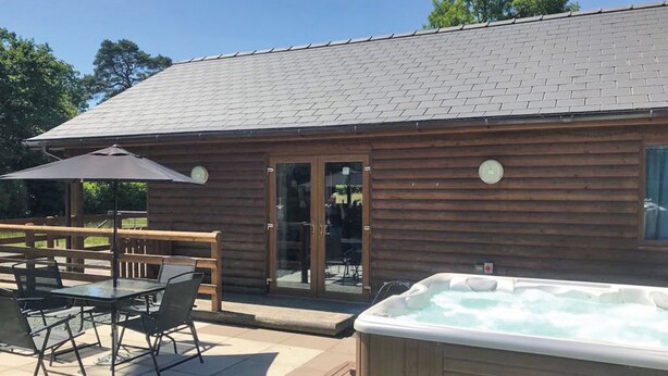 A wooden cabin with a hot tub, patio furniture, and a covered seating area. - Lodge with fantastic contemporary styling. (Llanddewi, Nr. Llandrindod Wells)