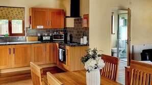 A kitchen with wooden cabinets, a dining table with chairs, a microwave, and a vase with flowers. - Lodge with fantastic contemporary styling. (Llanddewi, Nr. Llandrindod Wells)