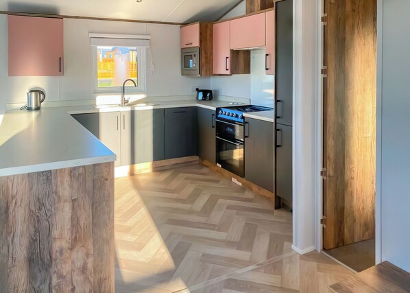 A modern kitchen with a herringbone wood floor, stainless steel appliances, and a large island.