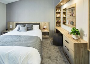 Une chambre moderne avec un grand lit, des tables de chevet, un bureau agrémenté d’une plante et des étagères intégrées.