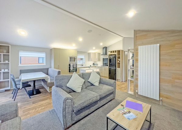 A modern living room with a sofa, a dining table, and a kitchen area in the background.