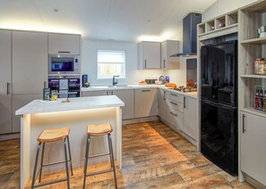 A modern kitchen with a central island, bar stools, a black refrigerator, and built-in appliances. - Pondview Retreat Lodge (Glenluce, Newton Stewart)