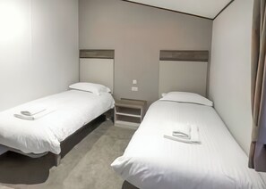 A twin room with two single beds, a small bedside table, and a wall-mounted shelf.