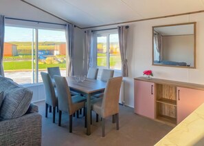 A room with a dining table, chairs, a sofa, a cabinet, and a large window with curtains.