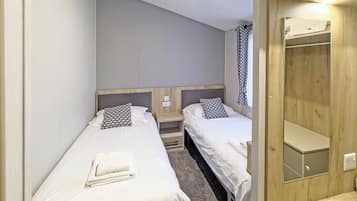 A room with two single beds, a wooden wardrobe, and a mirror.