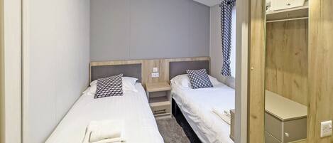 Een kamer met twee eenpersoonsbedden, een houten garderobe en een spiegel.