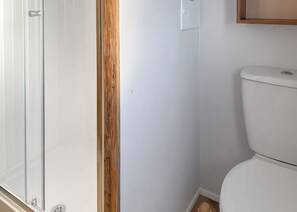 A bathroom with a white toilet, a wooden door frame, and a glass shower enclosure.