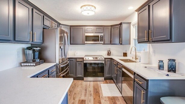 A modern kitchen with grey cabinets, stainless steel appliances, and a white countertop. - Beautiful Home Across the Street From ND (South Bend)