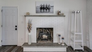 A white brick fireplace with a mantel shelf, a framed black and white photograph above it, and a white ladder to the right. - Beautiful Home Across the Street From ND (South Bend)
