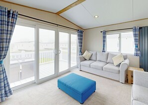 A room with a white sofa, blue curtains, a blue ottoman, and a view of a balcony.
