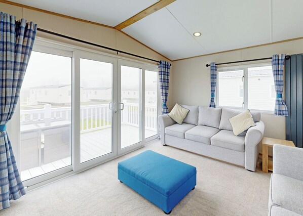 A room with a white sofa, blue curtains, a blue ottoman, and a view of a balcony.