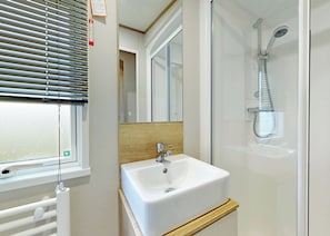 A bathroom with a white sink, a shower, and a window with blinds.
