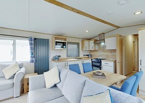 A compact kitchen with a microwave, stove, and sink. There is a dining area with a table and chairs.