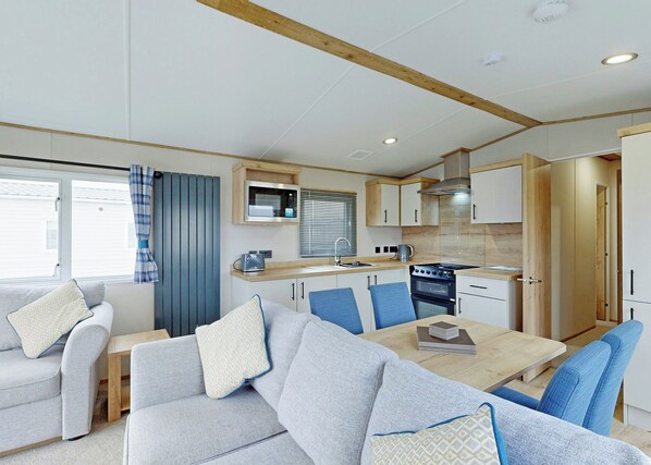 A compact kitchen with a microwave, stove, and sink. There is a dining area with a table and chairs.