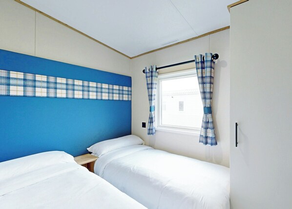 A room with two beds, a window with plaid curtains, and a blue accent wall.