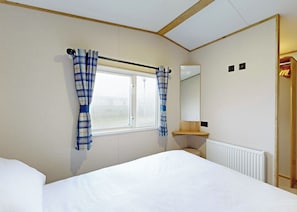 A bedroom with a bed, a window with curtains, a bedside table, a mirror, and a radiator.