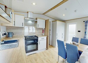 A modern kitchen with a stove, oven, and sink, wooden flooring, and a dining area with blue chairs.