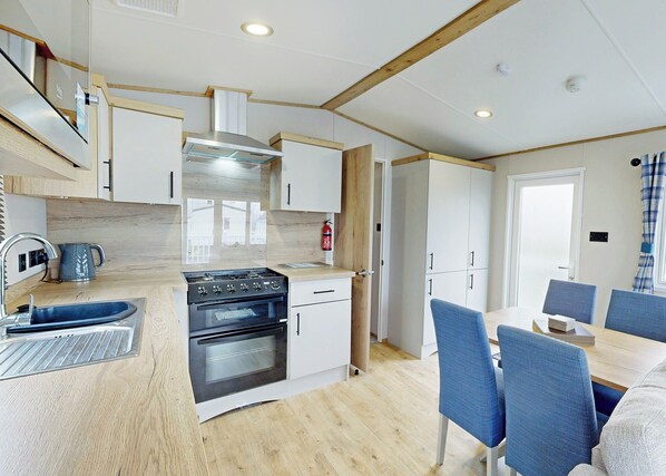 A modern kitchen with a stove, oven, and sink, wooden flooring, and a dining area with blue chairs.