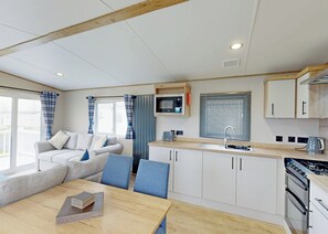 A modern kitchen with white cabinets, a microwave, and a stove. There is a dining area with a table and chairs.