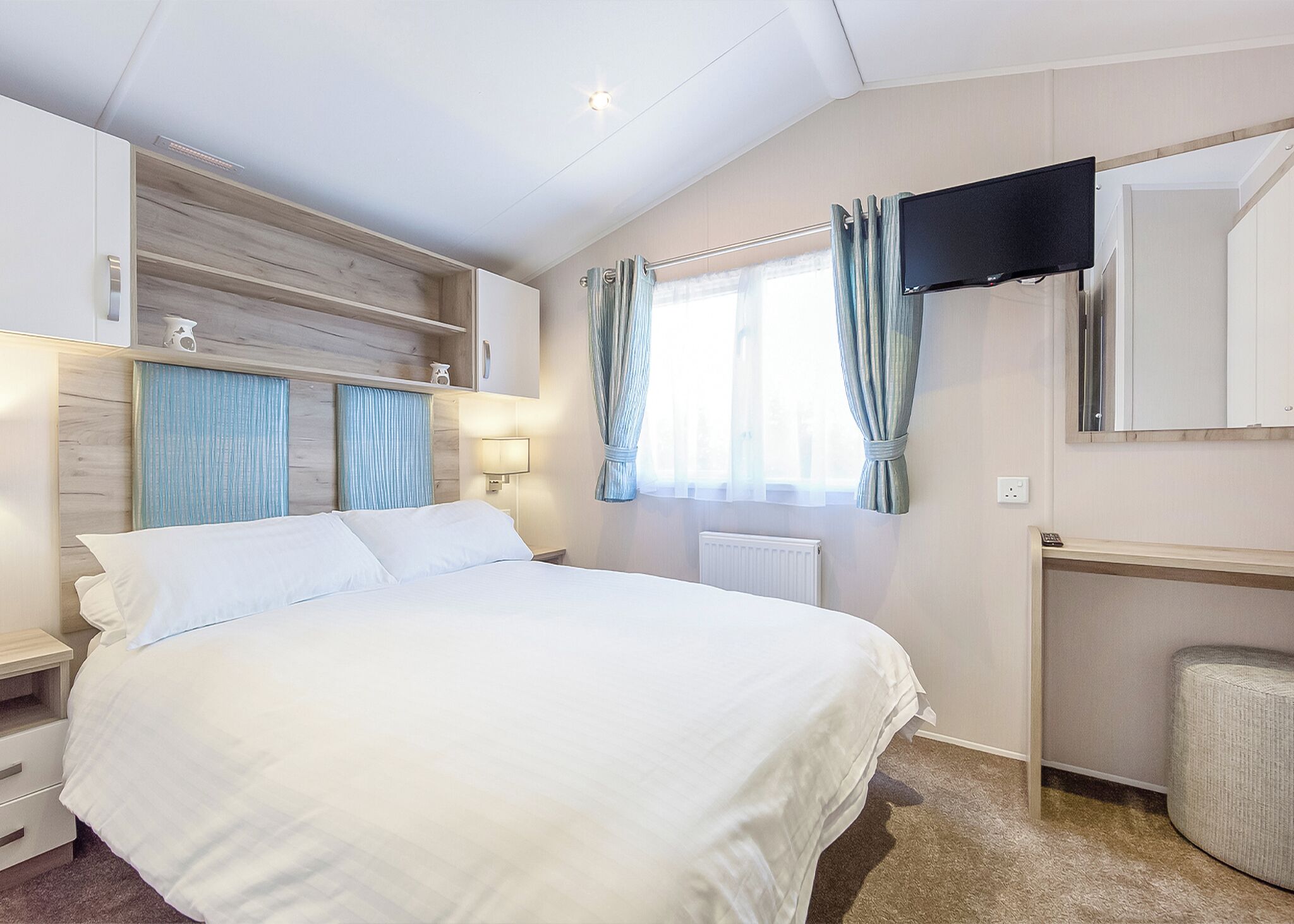 A hotel room with a bed, a TV mounted on the wall, a window with curtains, and a radiator.