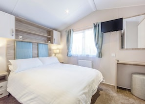 A hotel room with a bed, a TV mounted on the wall, a window with curtains, and a radiator.