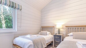 Ein Schlafzimmer mit zwei Betten, einem Fenster mit Blick auf Bäume, einem Heizkörper und einem Nachttisch mit Lampe.