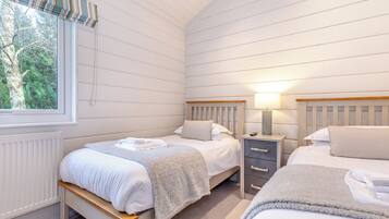 Een slaapkamer met twee bedden, een raam met uitzicht op bomen, een radiator en een nachtkastje met een lamp.
