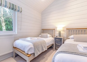A bedroom with two beds, a window with a view of trees, a radiator, and a bedside table with a lamp.