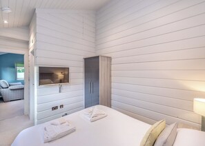 A hotel room with a bed, a TV mounted on the wall, a wardrobe, and a bathroom visible in the background.