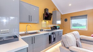 Une cuisine moderne avec des meubles gris, un évier, une cuisinière et un four à micro-ondes. Il y a une fenêtre donnant sur un paysage verdoyant et une horloge au mur.