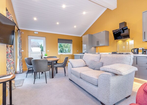A modern living room with a sofa, dining table, chairs, a TV, and a kitchen area with cabinets and appliances.
