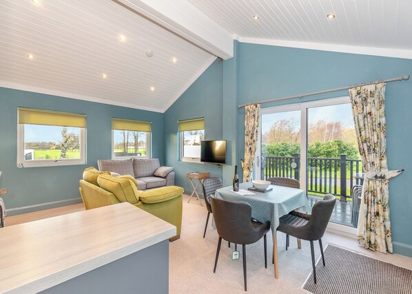 A room with a sofa, a dining table with chairs, a TV, and a balcony with curtains.