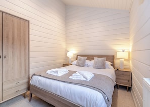 A bedroom with a wooden wardrobe, a bed with white linens, two bedside lamps, and a nightstand with a lamp. - 1 bedroom accommodation in Snainton Luxury Lodges (Snainton Luxury Lodges)