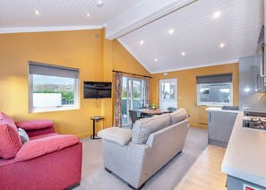 Ein modernes Wohnzimmer mit einer Couch, einem roten Sessel, einem Fernseher und einem Essbereich mit Tisch und Stühlen.