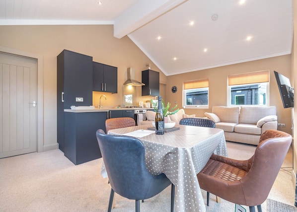 A modern kitchen with dark cabinets, a dining table with a polka dot tablecloth, and a sofa in the living area.