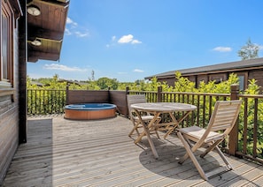 A wooden deck with a hot tub, a table, and two chairs. - Luxurious solid log lodge. (Wenhaston, Halesworth)